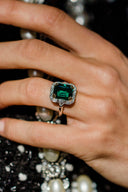 Hand wearing a ring with a green gemstone against a textured background