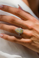 A close-up of a hand wearing a large pear-shaped yellow lab diamond ring.